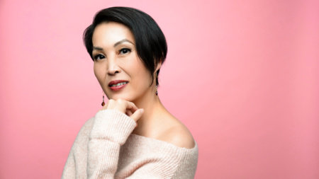 Author Stacey Lee poses for a portrait. She smiles and leans her chin on one hand.